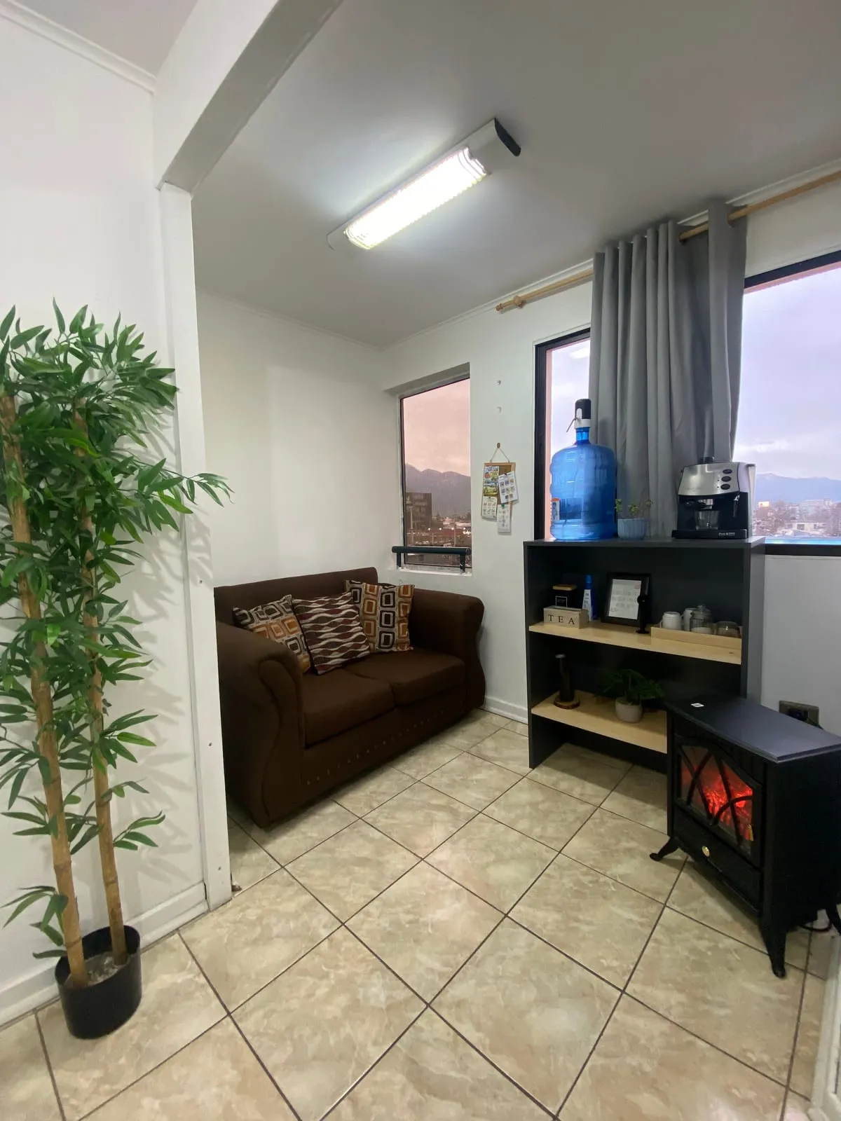 Sala de espera de FonoSer: un sofá, una planta, dispensador de agua y una ventana con vista a la cordillera