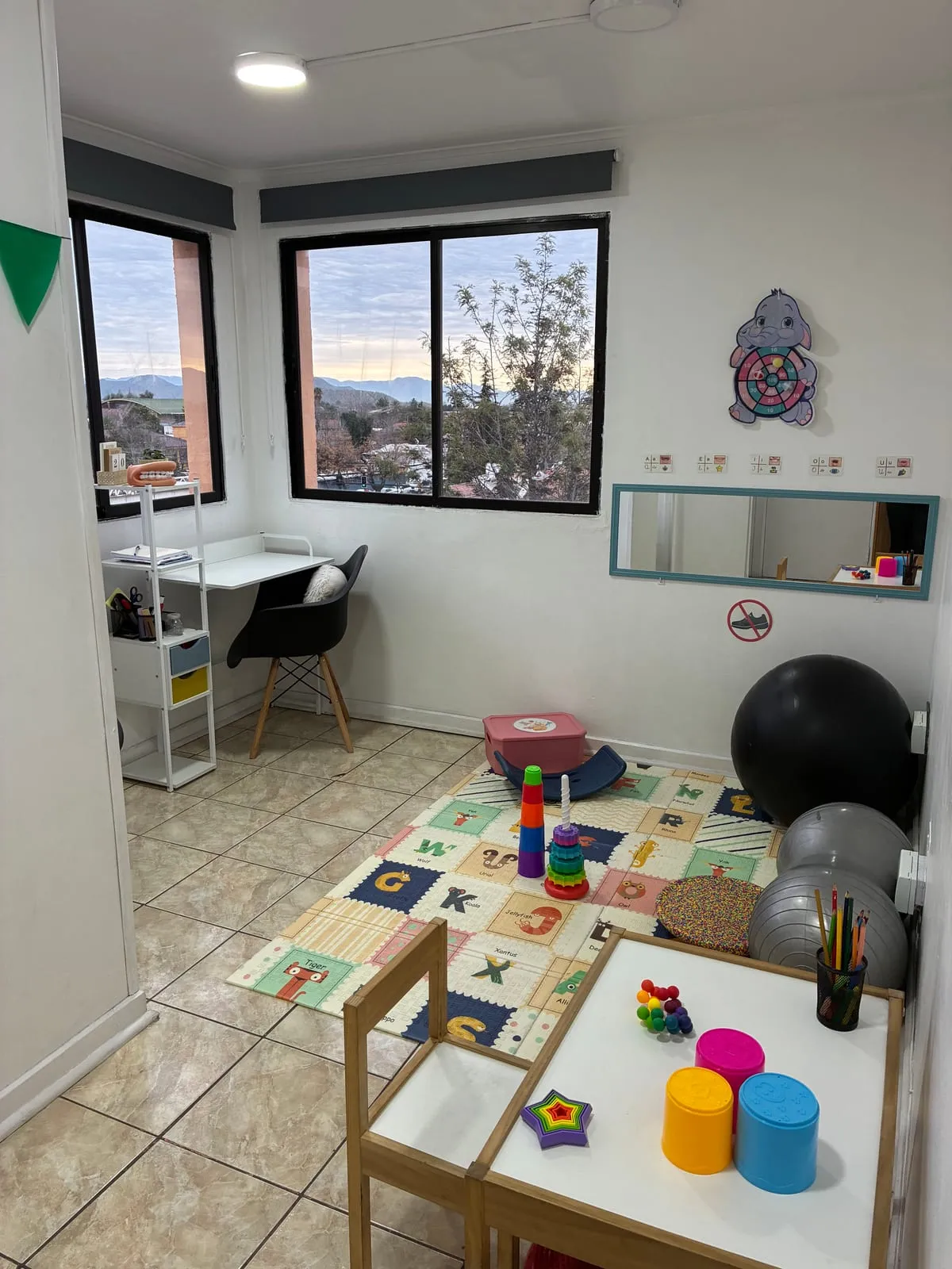 Sala de atención de FonoSer: alfombra de goma eva, mesa baja con material de juego, pelotas de terapia y un escritorio junto a la ventana